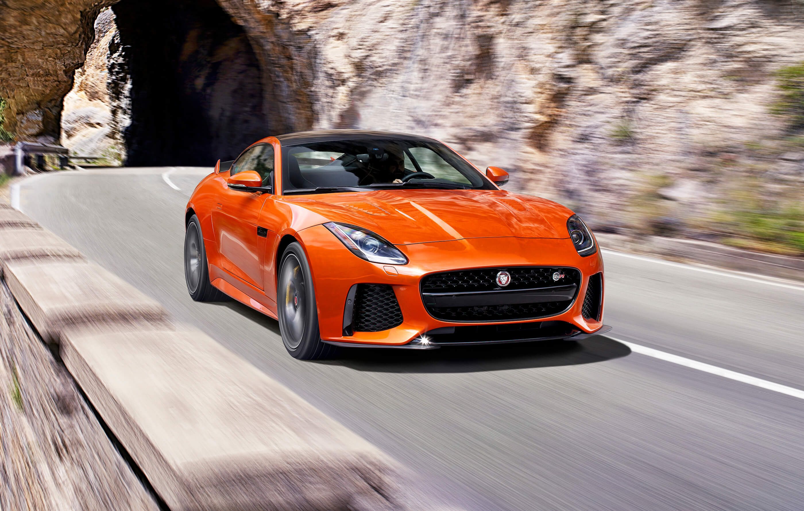 Full screen image of an orange Jaguar F-Type SVR on open roads