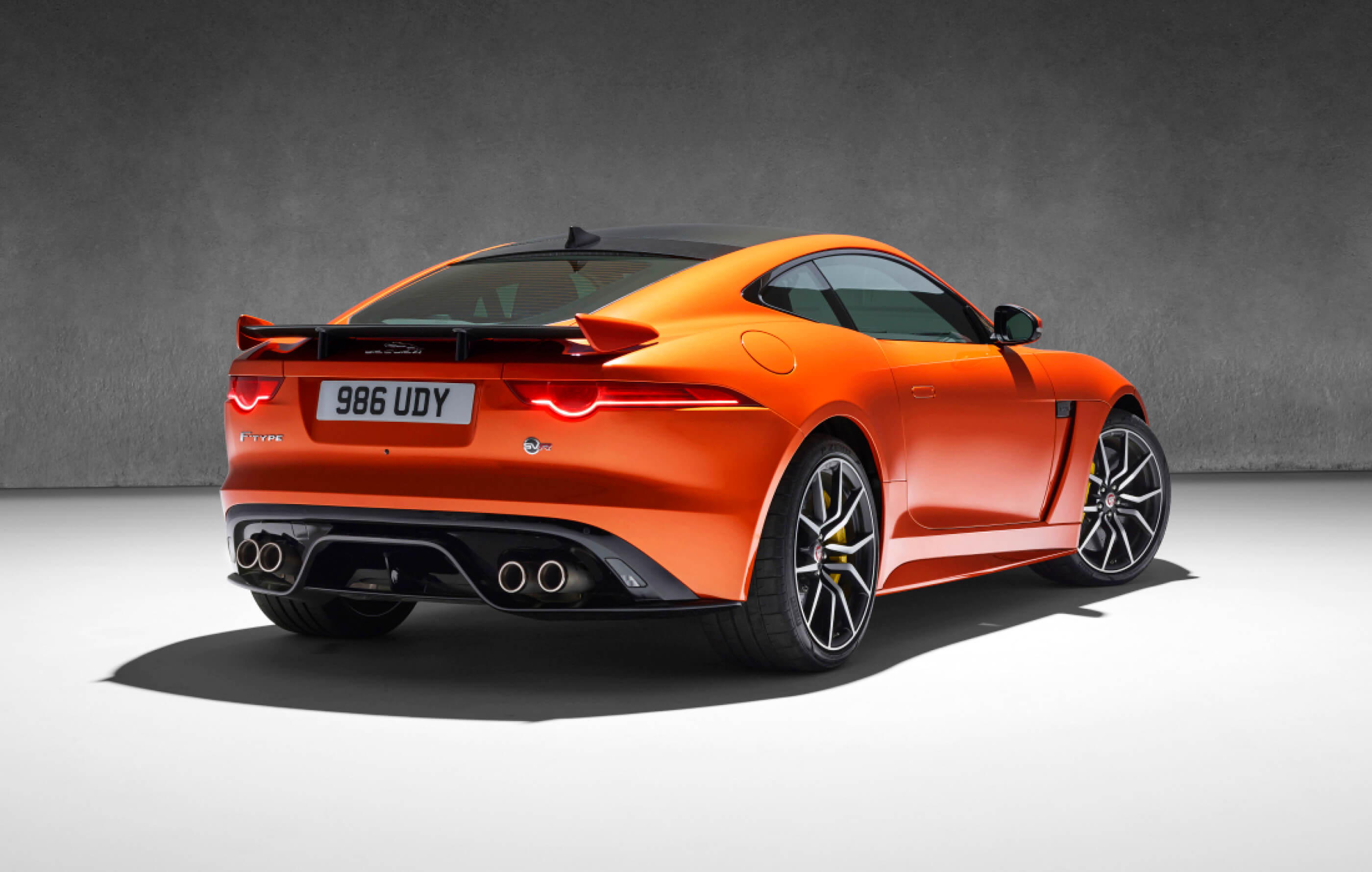Full screen image of an orange Jaguar F-Type SVR, with tan leather interior on an industrial charcoal background