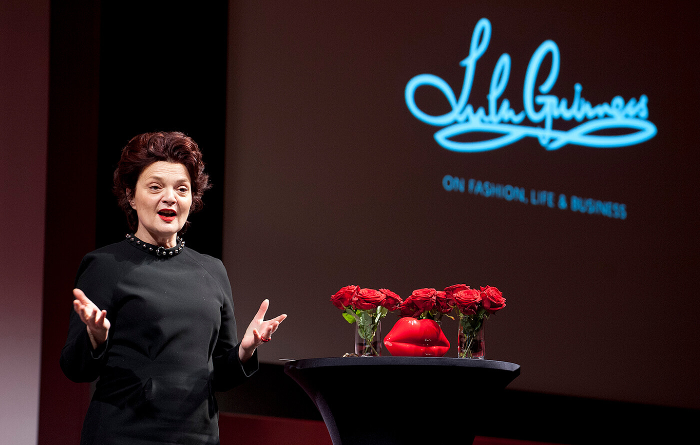 Guest speaker Lulu Guinness, dressed in black, speaking on stage about fashion, life and business