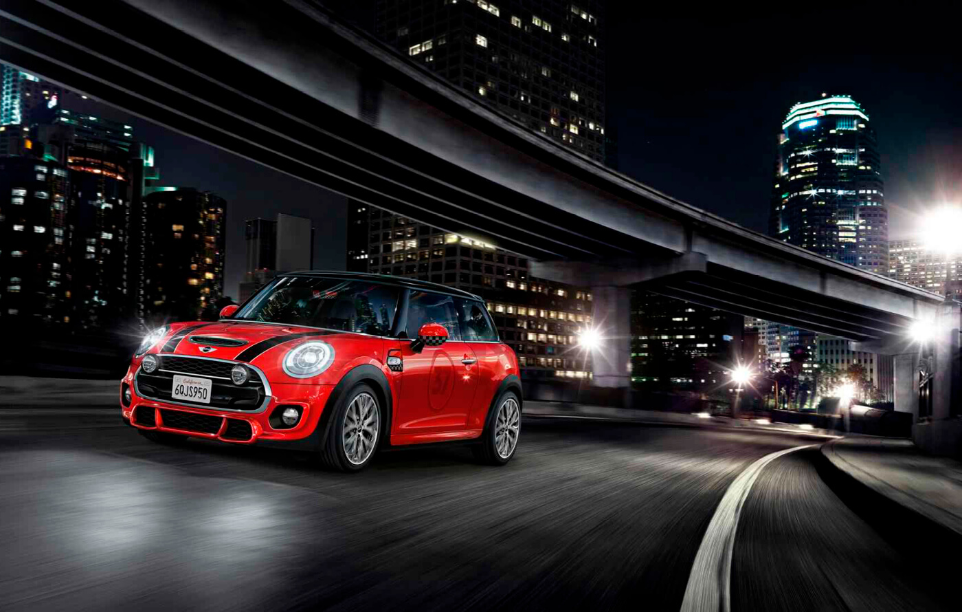 Full screen image of a red Mini John Cooper Works, racing along an urban street at night