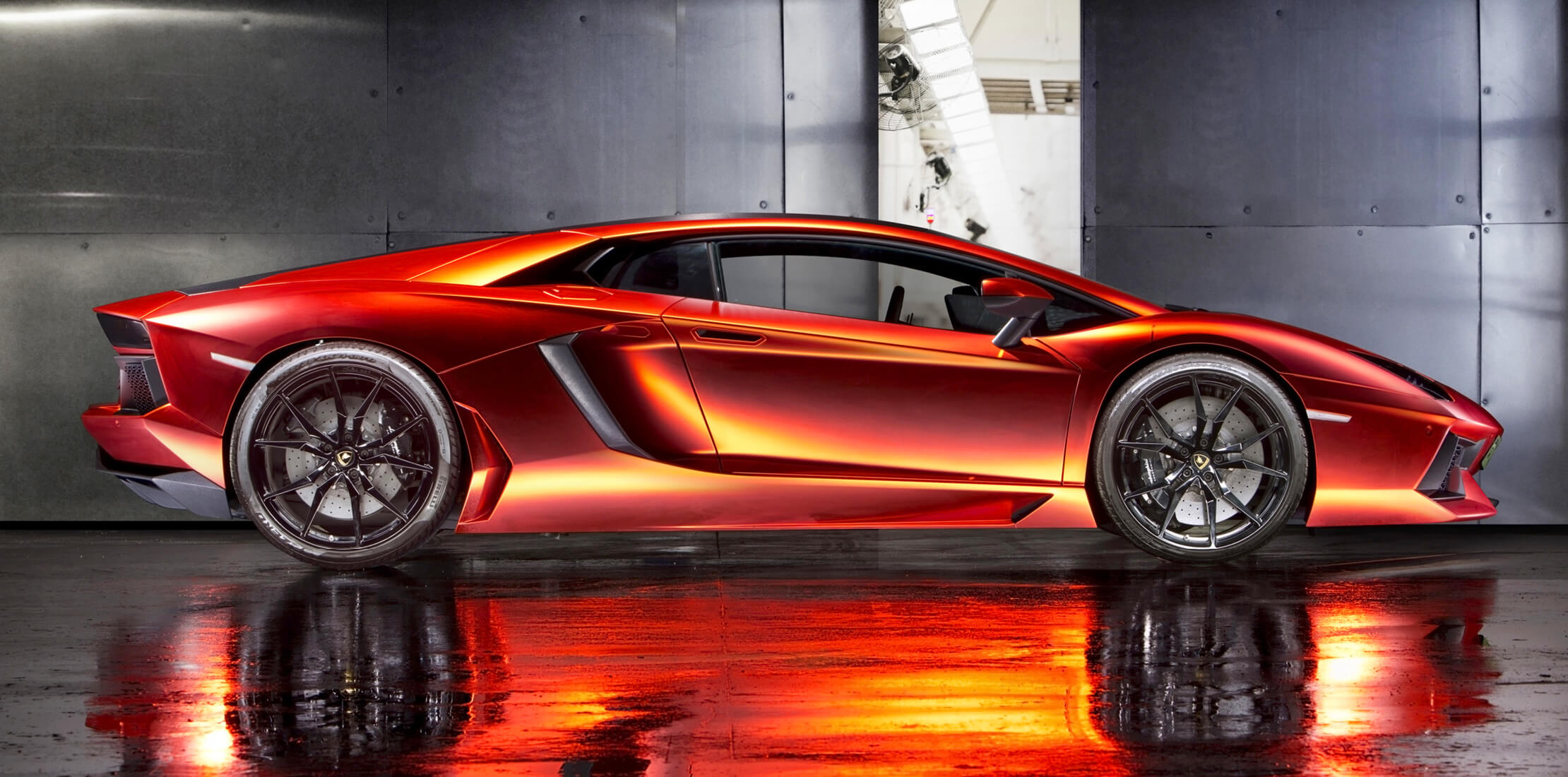 Profile shot of an orange Lamborghini Aventador Coupè with a dark concrete and metal backdrop