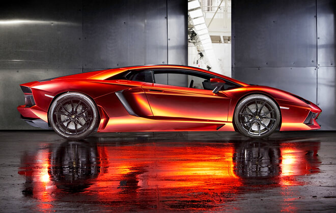 Profile shot of an orange Lamborghini Aventador Coupè with a dark concrete and metal backdrop